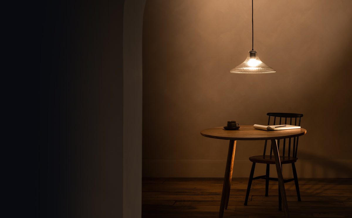 Dining table with a chair under a corston pendant light in a dimly lit room